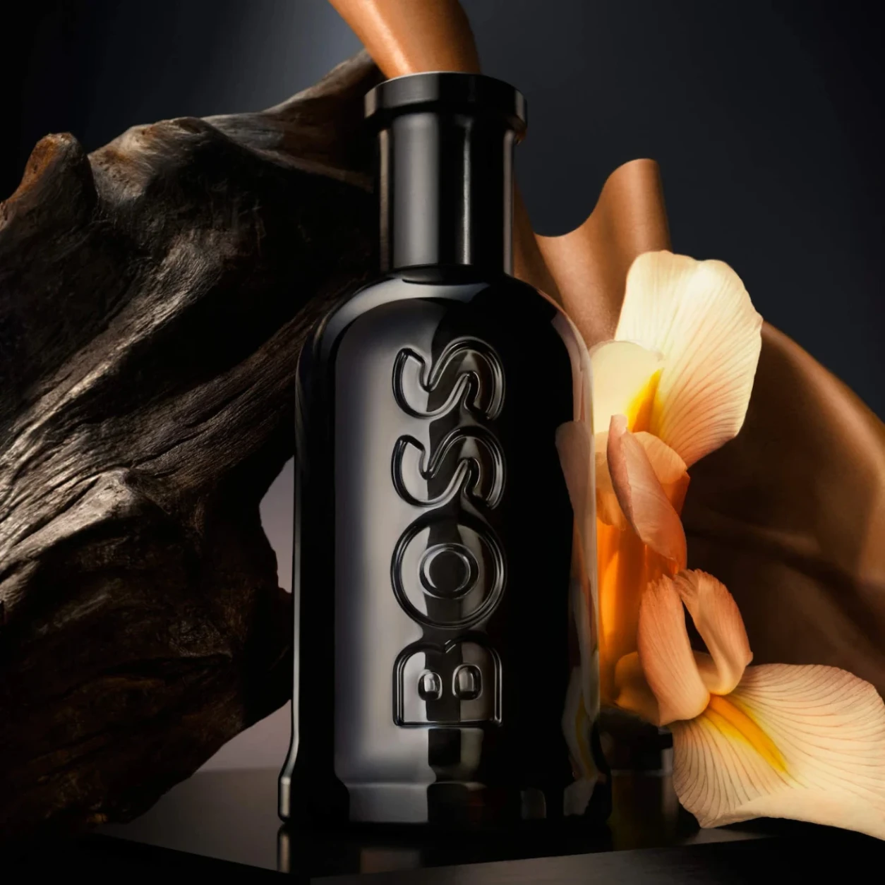 Black bottle with intricate design on a dark background with flowers